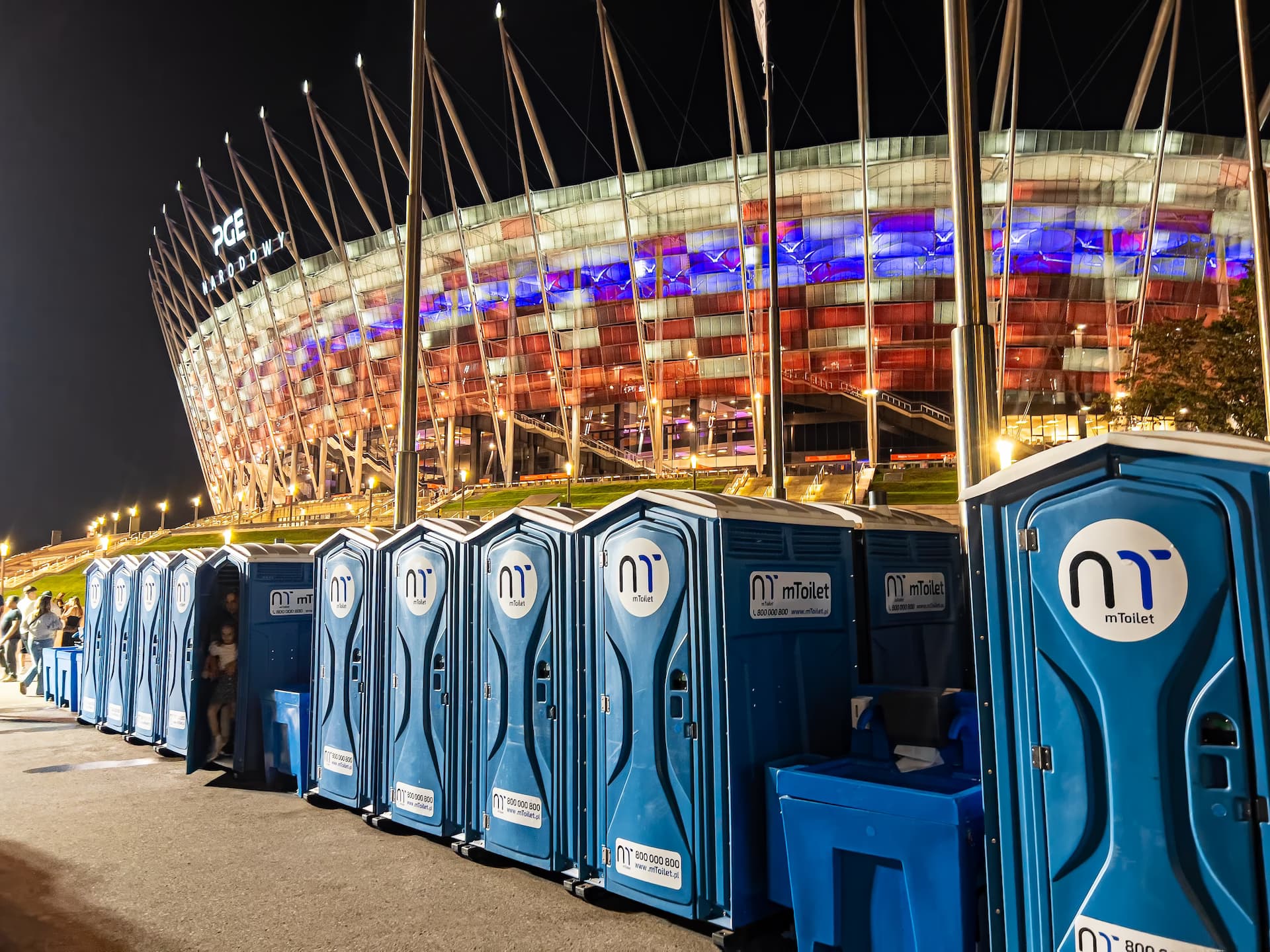 mToilet biotualetų eilė stadiono fone naktį